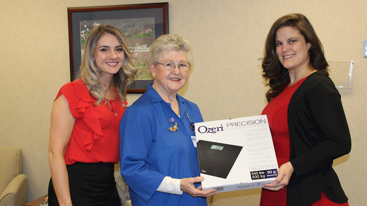 Progressive Care Unit Clinical Coordinator Allison Dietrich, Volunteer Bea Aikens, and Progressive Care Unit Nursing Director Adriana Palmer are shown holding a bathroom scale funded by the State Farm Companies Foundation Good Neighbor Grant.